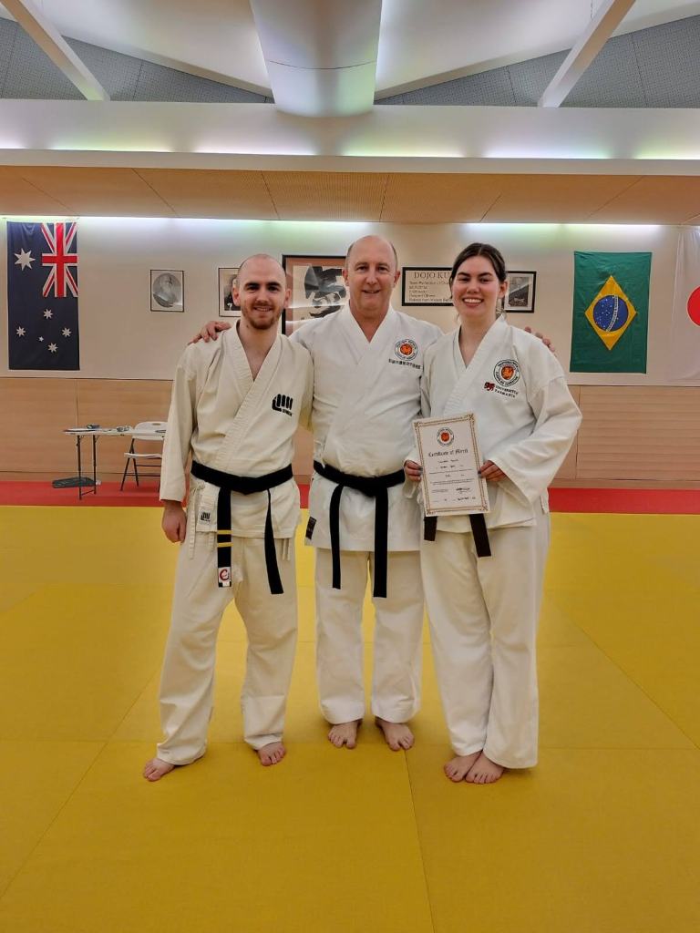 Two men and a woman in karate uniforms smile for the camera
