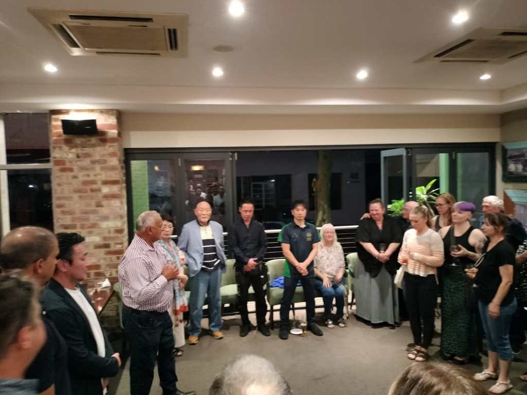 A group shot of people in casual clothing. They are gathering the night before the karate nationals begins. There are people of various ages and races. 