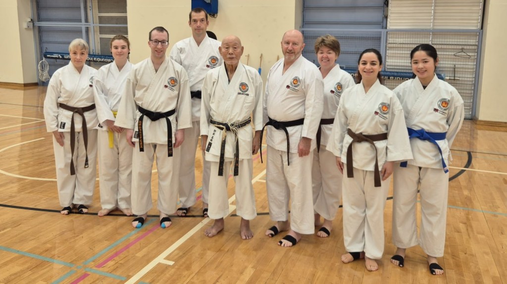 9 people pose with an older Japanese man, Takahashi Shihan. Most are smiling. 