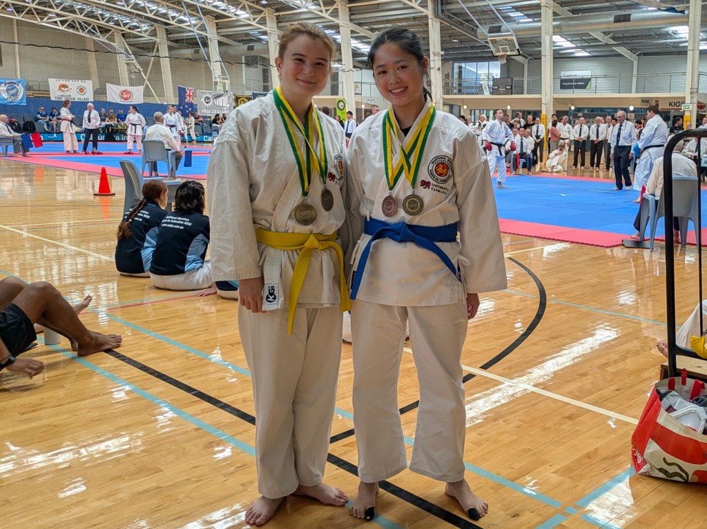 Two young women wearing karate uniforms and medals smile.